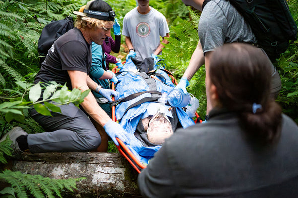 Wilderness EMT's Helping a Person in a forest setting by ventilating them with a bag valve mask and packaging them in a litter while protecting them from environment with a Hypothermia Wrap.