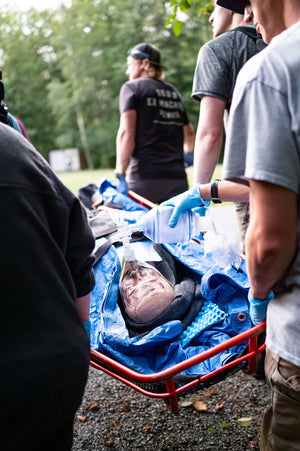 REMT students carrying a person on a stretcher with medical equipment, surrounded through a wilderness environment. 