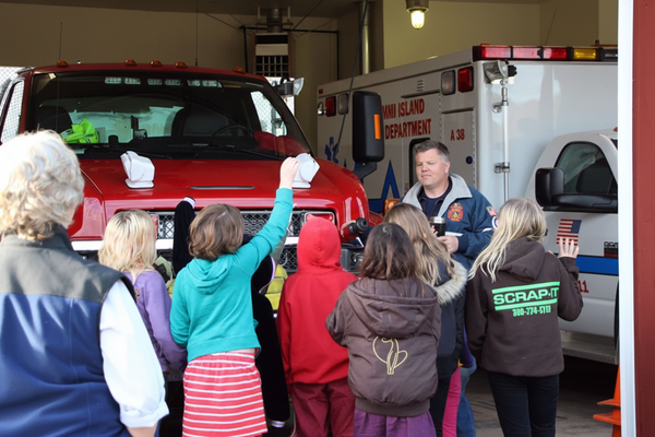 Group of people, including children, interacting with emergency vehicles in a garage setting.