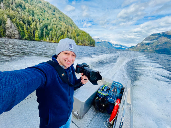 Wes Segar taking a selfie on a boat with a scenic mountain and lake background